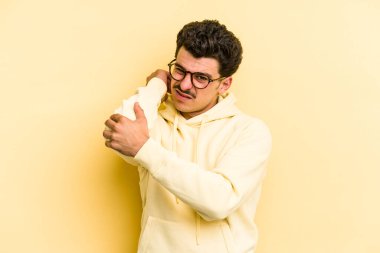 Sarı arka planda izole edilmiş genç beyaz bir adam stresten dolayı boynu ağrıyor, masaj yapıyor ve elle dokunuyor..