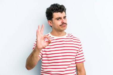 Kafkasyalı genç bir adam mavi arka planda izole edilmiş bir şekilde göz açıp kapayana kadar iyi bir el hareketi yapıyor..