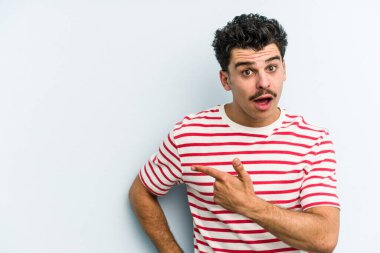 Mavi arka planda izole edilmiş genç beyaz adam yan tarafı işaret ediyor.