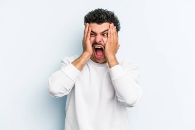 Kafkasyalı genç adam mavi arka planda izole edilmiş kulakları kulaklarıyla kapatıyor çok fazla ses duymamaya çalışıyor..