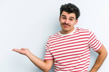 Mavi arka planda izole edilmiş genç beyaz bir adam bir palmiye üzerinde fotokopi alanı ve belinde bir el daha gösteriyor..