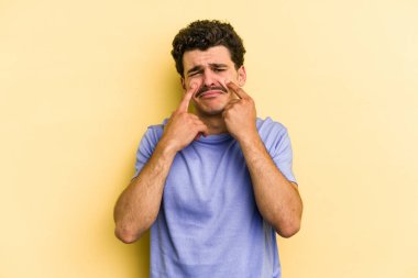 Kafkasyalı genç adam sarı arka planda izole edilmiş, ağlıyor, bir şeyden memnun değil, acı ve kafa karışıklığı kavramı..