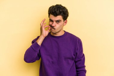 Sarı arka planda izole edilmiş genç beyaz bir adam parmakları dudaklarında bir sır saklıyor..