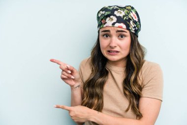 Mavi arka planda izole edilmiş genç beyaz kadın işaret parmağıyla fotokopi alanını işaret ederek şok oldu..