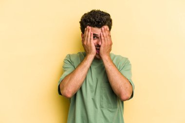 Sarı arka planda izole edilmiş genç beyaz adam yüzünün yarısını palmiye ile örterek eğleniyor..