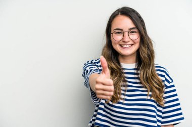 Beyaz arka planda izole edilmiş genç beyaz kadın gülümsüyor ve başparmağını kaldırıyor.