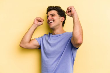 Sarı arka planda izole edilmiş genç beyaz adam özel bir günü kutluyor, atlıyor ve enerjiyle kollarını kaldırıyor..