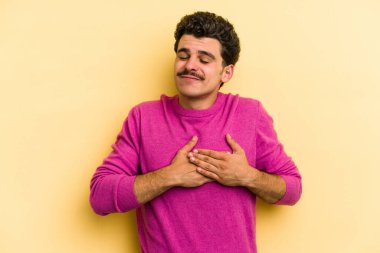 Sarı arka planda izole edilmiş beyaz bir genç, dost canlısı bir ifadeye sahip, avuçlarını göğsüne bastırıyor. Aşk konsepti.
