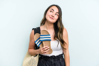 Young caucasian woman holding sandals isolated on blue background dreaming of achieving goals and purposes