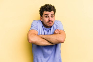 Sarı arka planda izole edilmiş genç beyaz adam omuzlarını silkeliyor ve gözleri açık..