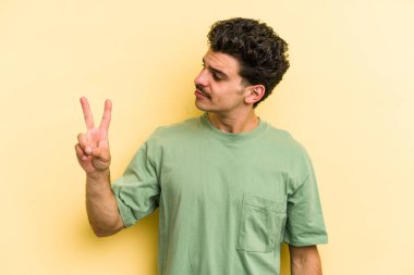 Sarı arka planda izole edilmiş genç beyaz adam neşeli ve kaygısız parmakları olan bir barış sembolü gösteriyor..