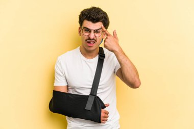 Young caucasian man with broke hand isolated on yellow background showing a disappointment gesture with forefinger.