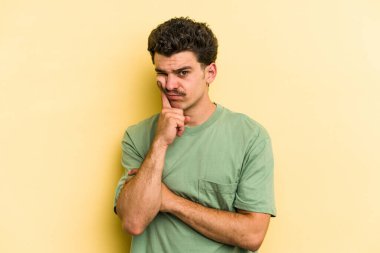Sarı arka planda izole edilmiş genç beyaz adam alaycı bir ifadeyle kameraya bakıyor..