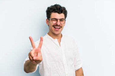 Mavi arka planda izole edilmiş genç beyaz adam iki numarayı parmaklarıyla gösteriyor..