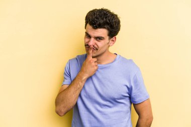 Kafkasyalı genç adam sarı arka planda izole edilmiş düşünüyor ve yukarı bakıyor, yansıtıyor, düşünüyor, hayal kuruyor..