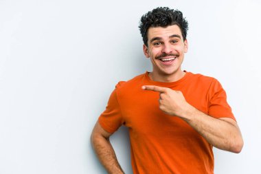 Mavi arka planda izole edilmiş genç beyaz adam işaret parmağıyla işaret ederek gülümsüyor..