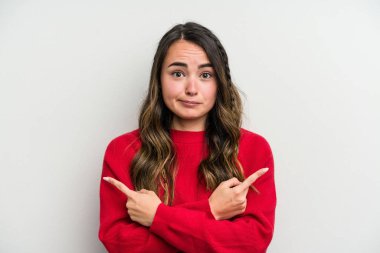 Beyaz arka plan noktalarında izole genç beyaz kadın, iki seçenek arasında seçim yapmaya çalışıyor.