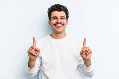 Mavi arka planda izole genç beyaz adam işaret iki ön parmakları boş bir boşluk gösteren.