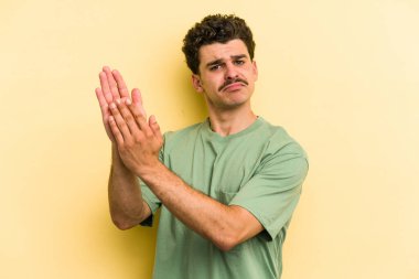 Sarı arka planda izole edilmiş genç beyaz adam enerjik ve rahat hissediyor, ellerini ovuşturuyor kendinden emin..