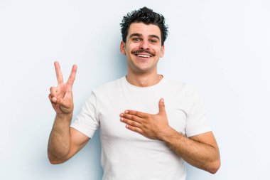 Kafkasyalı genç adam mavi arka planda izole edilmiş yemin ediyor, elini göğsüne koyuyor..