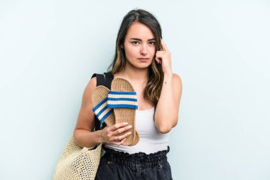 Young caucasian woman holding sandals isolated on blue background pointing temple with finger, thinking, focused on a task.