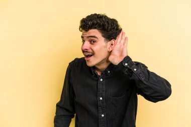 Sarı arka planda izole edilmiş genç beyaz bir adam bir dedikoduyu dinlemeye çalışıyor..