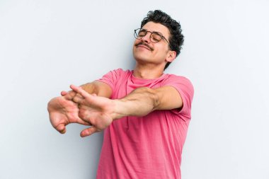 Mavi arka planda izole edilmiş genç beyaz adam kollarını uzatıyor, rahat bir konumda..