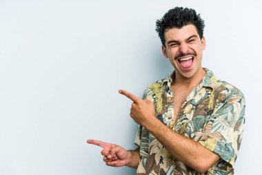 Mavi arka planda izole edilmiş genç beyaz adam işaret parmağıyla fotokopi alanını işaret ederek heyecan ve arzusunu ifade ediyor..