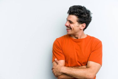 Mavi arka planda izole edilmiş genç beyaz adam kollarını kavuşturarak gülümsüyor..