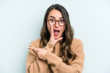 Kafkasyalı genç bir kadın mavi arka planda izole edilmiş. Dedikodu yapıyor, bir şeyleri bildiriyor..