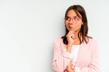 Genç İspanyol kadın mavi arka planda yalnız mutlu ve kendinden emin gülümsüyor, elleriyle çenesine dokunuyor..