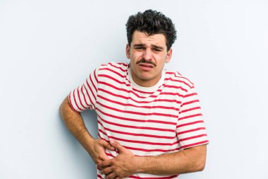 Mavi arka planda karaciğer ağrısı çeken, karnı ağrıyan genç beyaz bir adam..