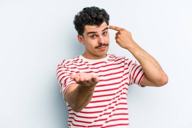 Kafkasyalı genç adam mavi arka planda izole edilmiş ve elinde bir ürün tutuyor..