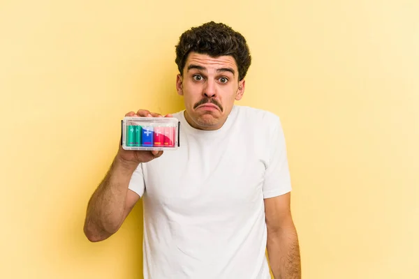 Young Caucasian Man Holding Batteries Isolated Yellow Background Shrugs Shoulders — 图库照片