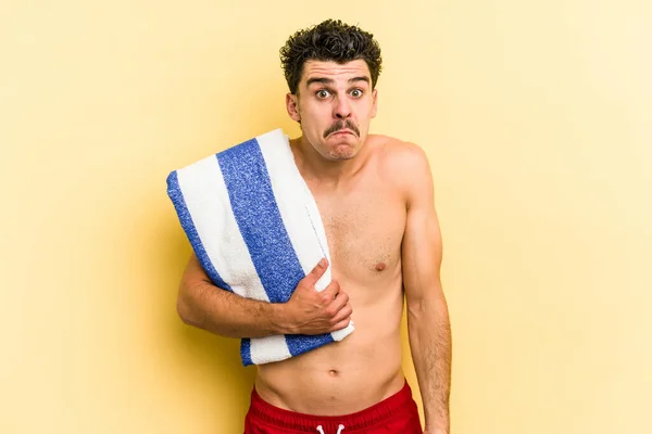 Young Caucasian Man Holding Beach Towel Isolated Yellow Background Shrugs — Photo