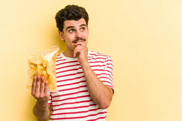 Young Caucasian Man Holding Bag Chips Isolated Yellow Background Relaxed — Foto de Stock