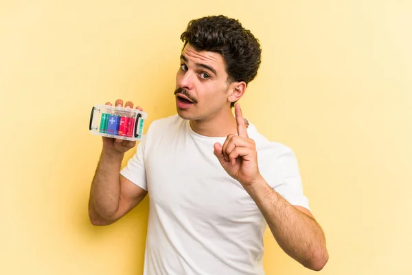 Young Caucasian Man Holding Batteries Isolated Yellow Background Having Idea — Stock Fotó