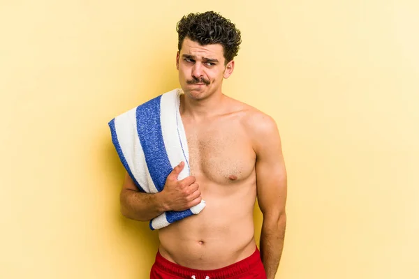 Young Caucasian Man Holding Beach Towel Isolated Yellow Background Confused — 图库照片