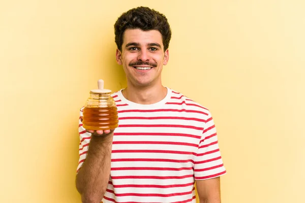 Young Caucasian Man Holding Honey Jar Isolated Yellow Background Happy — Zdjęcie stockowe