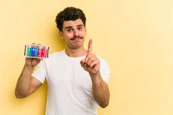 Young Caucasian Man Holding Batteries Isolated Yellow Background Showing Number — Foto de Stock