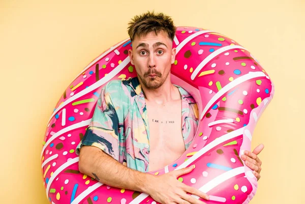 Young Caucasian Man Holding Inflatable Donut Isolated Yellow Background Shrugs — 图库照片