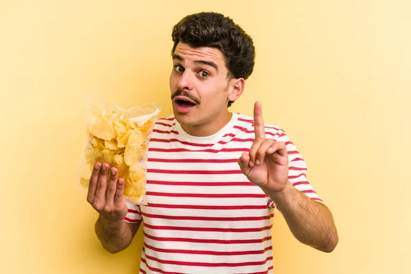 Young Caucasian Man Holding Bag Chips Isolated Yellow Background Having — Stockfoto