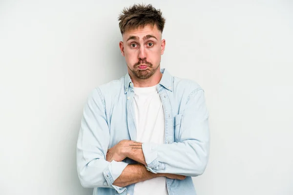 Young caucasian man isolated on white background blows cheeks, has tired expression. Facial expression concept.