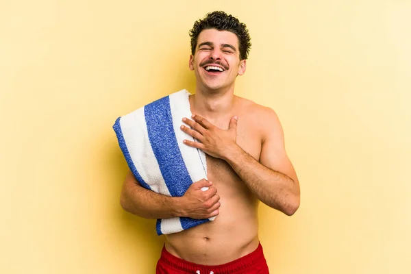 Young Caucasian Man Holding Beach Towel Isolated Yellow Background Laughs —  Fotos de Stock