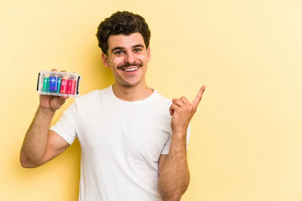 Young Caucasian Man Holding Batteries Isolated Yellow Background Smiling Pointing — Foto Stock