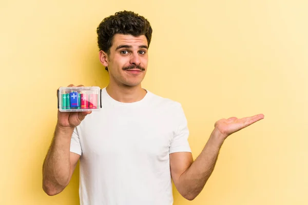 Young Caucasian Man Holding Batteries Isolated Yellow Background Showing Copy — Foto Stock