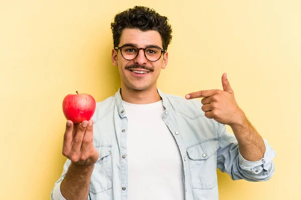 Young Caucasian Man Holding Apple Isolated Yellow Background Person Pointing — ストック写真
