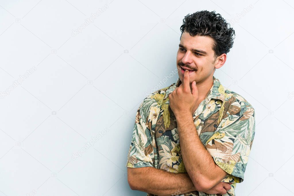 Young caucasian man isolated on blue background relaxed thinking about something looking at a copy space.