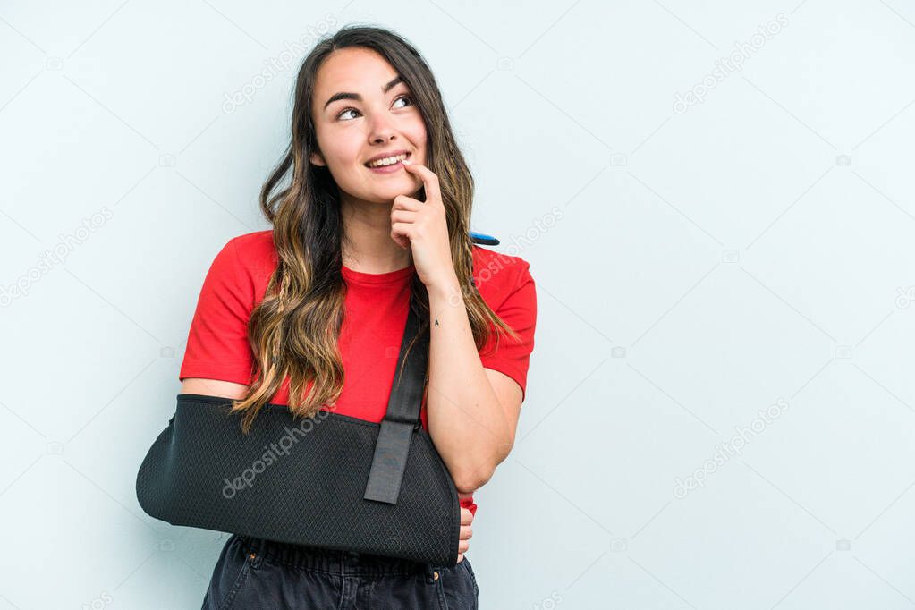 Young caucasian woman with broke hand isolated on blue background relaxed thinking about something looking at a copy space.