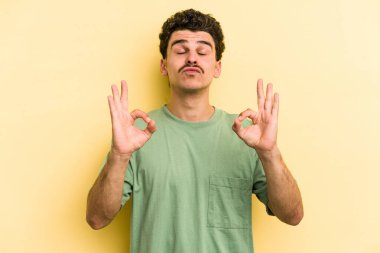 Sarı arka planda izole edilmiş genç beyaz adam sıkı çalışma gününden sonra rahatlıyor. Yoga yapıyor..